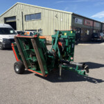 Industrial building with corrugated metal siding, green machinery in foreground, and a white Russell Vans/vehicle parked outside.