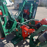 Close-up of green and red agricultural planter machinery with hydraulic components and hoses visible in a yard.