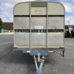 Rear view of a large beige trailer on a blue hitch, with a Bateson Trailers logo visible, in a parking lot.