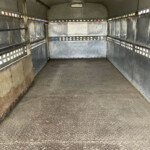 Empty metal trailer interior with diamond-plate floor and riveted panels along the walls, small rectangular vents along the sides.