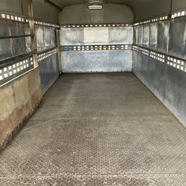 Empty metal trailer interior with diamond-plate floor and riveted panels along the walls, small rectangular vents along the sides.