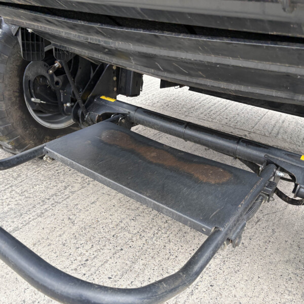 Close-up of a heavy-duty trailer undercarriage showing a large off-road tire, wheel hub, and metal frame.