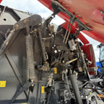 Close-up of exposed hydraulic hoses, linkages, and wiring inside red agricultural machinery frame.
