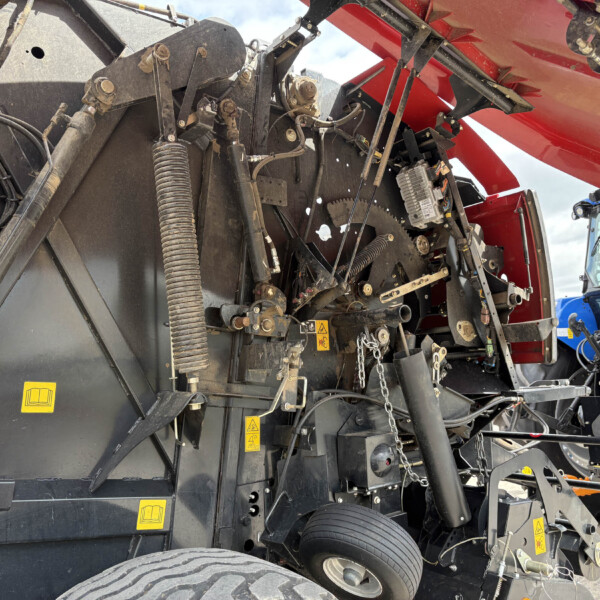 Close-up of exposed mechanical components inside a red agricultural harvester, including gears, hoses, and hydraulic cylinders.
