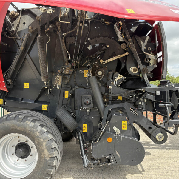 Rear view of a red agricultural machine with exposed gears, hoses, and wiring visible inside the body panel.