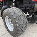 Close-up of a large off-road tire on a heavy-duty vehicle, with black chassis and mechanic components in the background.