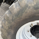 Close-up of a muddy motorcycle tire and rim with dirt on the tread and wheel bolts visible.