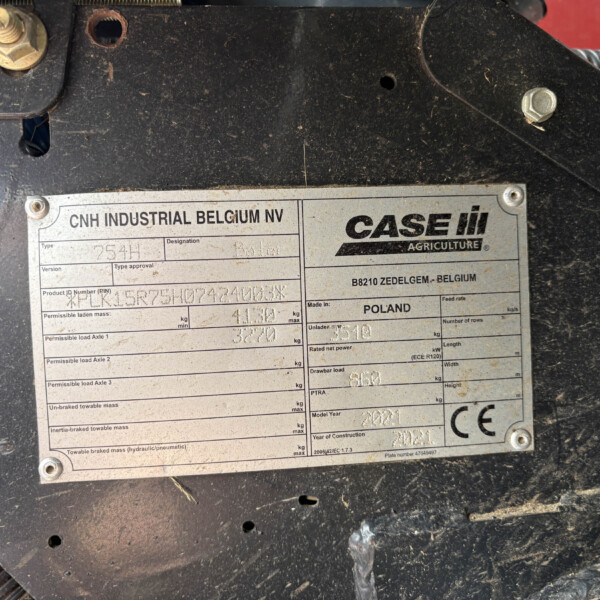 Metal identification/data plate on dirty black machinery showing CNH INDUSTRIAL BELGIUM NV and CASE IH Agriculture branding, with model and specification fields visible.