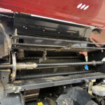 Close-up of the inner mechanism of a red agricultural machine, showing belts, black metal frames, and hydraulic components.