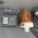 Top-down view of a control panel with keypad and a large orange warning beacon surrounded by wires and a black surface surface edge.