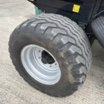 Close-up of a large off-road tire with deep zigzag tread on a heavy vehicle, resting on a paved surface.