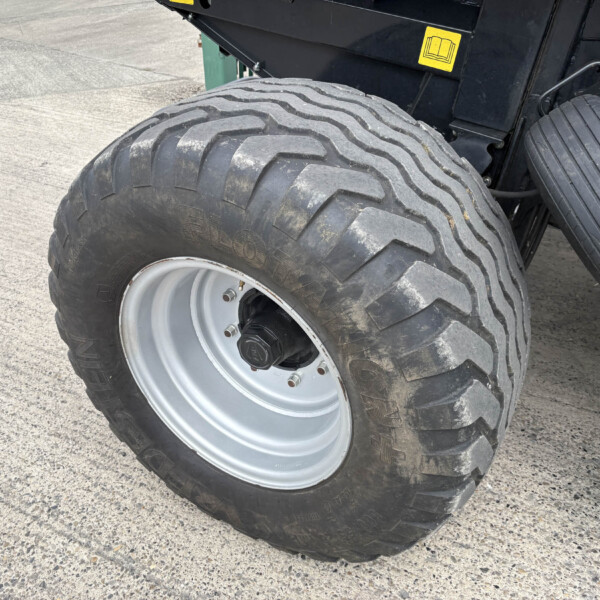 Close-up of a large off-road tire with deep zigzag tread on a heavy vehicle, resting on a paved surface.