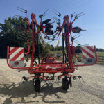 Red agricultural implement with multiple tines and wheels outdoors, likely a root harvester, branded Kverneland, under a blue sky.