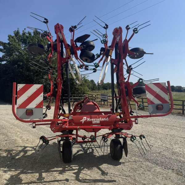 Red agricultural implement with multiple tines and wheels outdoors, likely a root harvester, branded Kverneland, under a blue sky.
