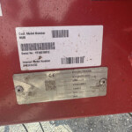 Close-up of a red metal surface with a white label showing Cust. Model Number 8590 and Serial No. VF69310812, plus a barcode.