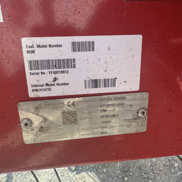 Close-up of a red metal surface with a white label showing Cust. Model Number 8590 and Serial No. VF69310812, plus a barcode.