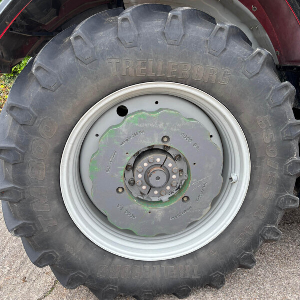 Close-up of a large tractor rear tire and wheel, showing the bulky tread and metal rim with a green center plate under a red fender.