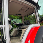 Interior of an open truck cab featuring the driver's seat and dashboard, with the door and step visible on the left and a red exterior panel in the foreground.