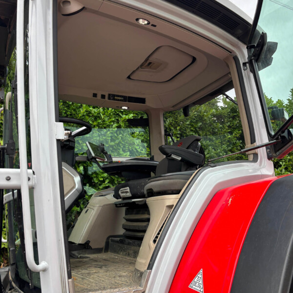 Interior of an open truck cab featuring the driver's seat and dashboard, with the door and step visible on the left and a red exterior panel in the foreground.