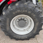 Close-up of a tractor rear tire and rim, with deep treads and the marking 650/65R28, red tractor body in the background.