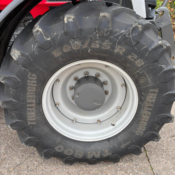 Close-up of a tractor rear tire and rim, with deep treads and the marking 650/65R28, red tractor body in the background.