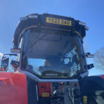 Front view of a red vehicle cab with the door open, exposing the control panel and yellow license plate reading YX22 DAO against a blue sky.