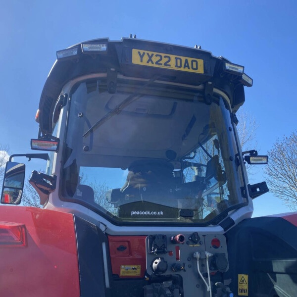 Front view of a red vehicle cab with the door open, exposing the control panel and yellow license plate reading YX22 DAO against a blue sky.