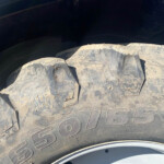 Close-up of a dusty off-road tire with a white rim, showing tread and sidewall markings.