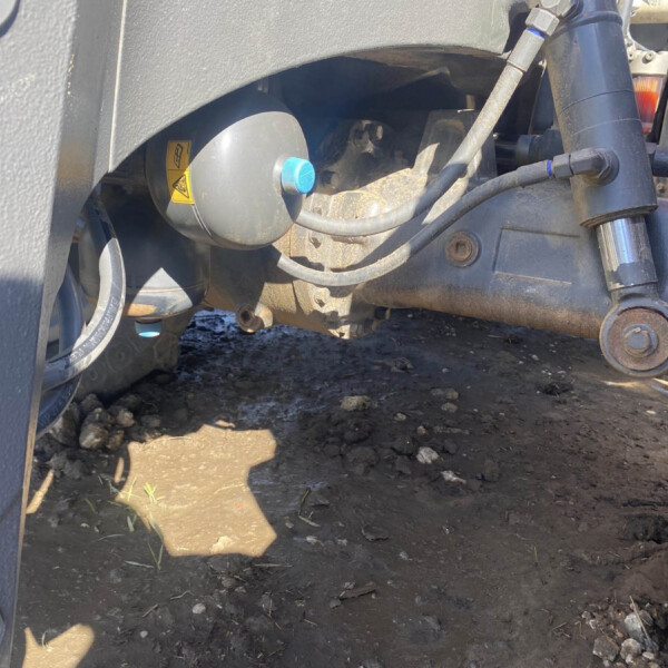 Close-up of a heavy machine's undercarriage showing hoses, a blue cap, and a warning sticker on a round component.