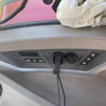 Close-up of a car dashboard with control buttons, a coiled cord hanging down, and a crumpled light cloth near the windshield edge.