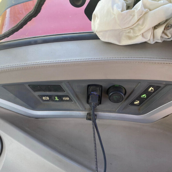 Close-up of a car dashboard with control buttons, a coiled cord hanging down, and a crumpled light cloth near the windshield edge.