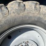 Close-up of a muddy off-road tire with chunky tread and a steel wheel rim visible at the bottom.