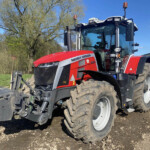 Red Massey Ferguson tractor on a muddy dirt surface, with a large front attachment, under a clear blue sky.