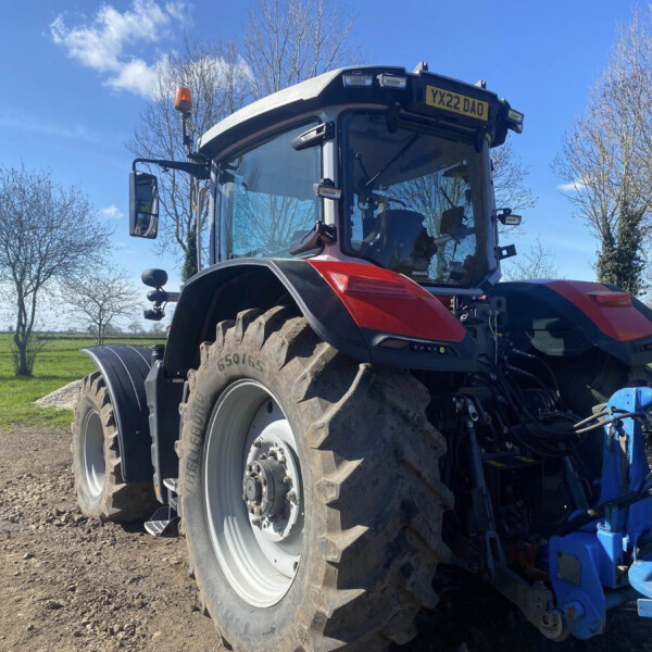 Close-up of a red tractor with large rear tire, blue attachments, and a yellow license plate reading 'YX22 DAO' under a blue sky.