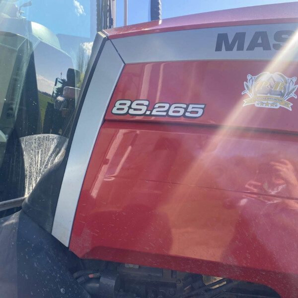 Close-up of a red truck cab showing the number 85.265 and a crest-style logo on the door, with the windshield and side panel visible and sun glare across the image.