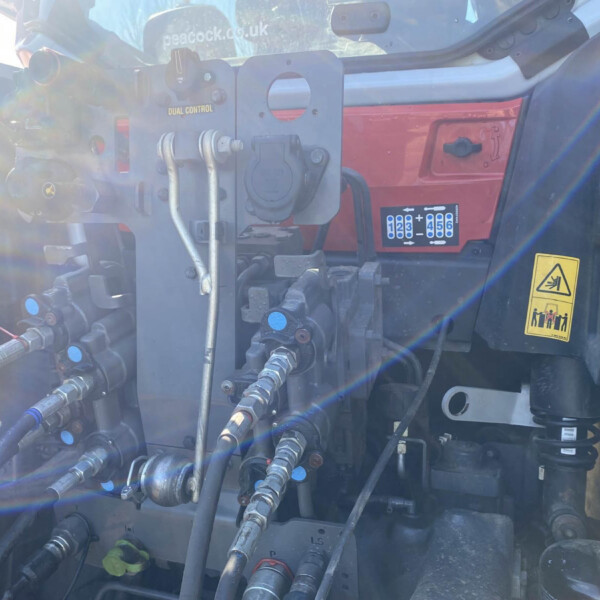 Close-up of a hydraulic control panel with hoses and metal fittings, sun glare over the machinery inside a heavy vehicle cab.