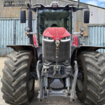 Front view of a red tractor with oversized rear tires, parked before a corrugated metal wall.