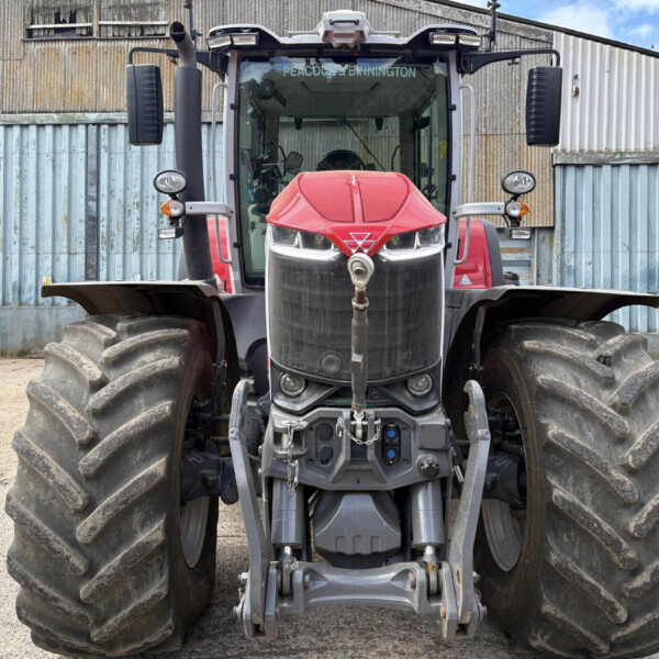 Front view of a red tractor with oversized rear tires, parked before a corrugated metal wall.