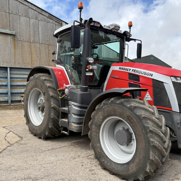 Red Massey Ferguson tractor with large front tires parked beside a corrugated metal building, front view showing cabin and orange beacon lights.