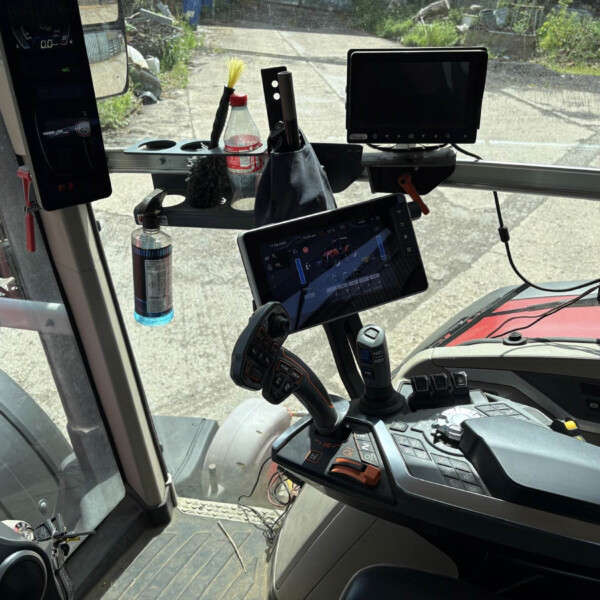 Interior of a truck cab with multiple screens, a tablet mounted on the console, a water bottle, a brush, and various controls on the dash.