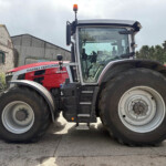 Red Massey Ferguson tractor front with oversized tires in a farmyard setting; buildings in the background and orange beacon on top of cab.