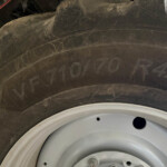 Close-up of a dark tire with a white wheel rim, showing dirt, scratches, and faint markings on the sidewall.