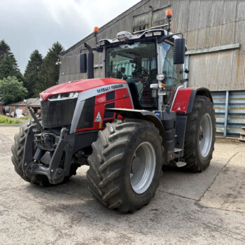 Red Massey Ferguson tractor parked in a yard beside a corrugated metal industrial building.