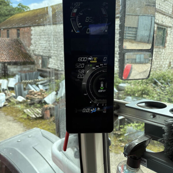 Vertical digital instrument panel in a truck cab with gauges visible, plus a side mirror and cleaning bottle nearby outside the window.