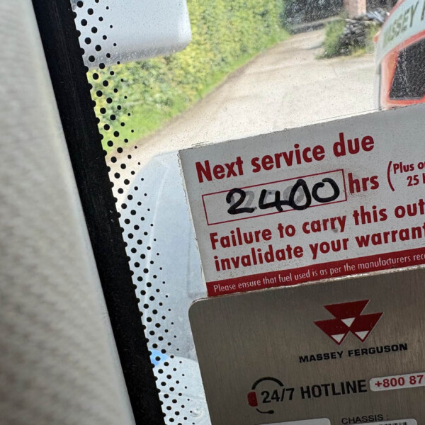 Close-up of a maintenance sticker on a vehicle panel reading 'Next service due' with a Massey Ferguson logo and a 24/7 hotline visible.