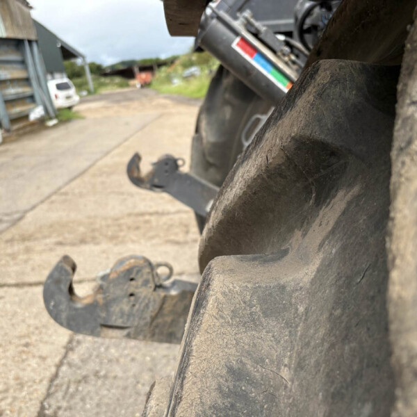 Close-up of a large dusty tire tread with industrial equipment and a yard in the blurred background