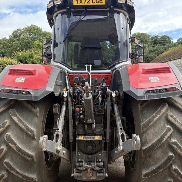 Rear view of a red tractor with large muddy tires and exposed hydraulic hitch system.