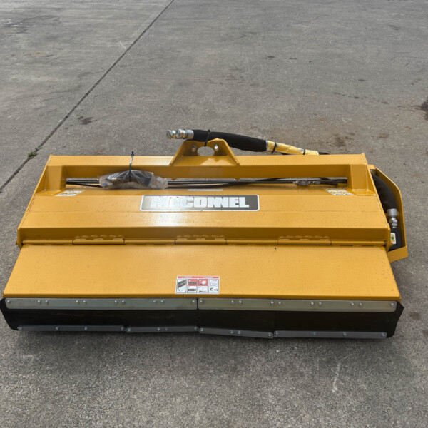 Yellow industrial hydraulic attachment on a concrete surface, showing hoses and mounting frame with warning labels visible.