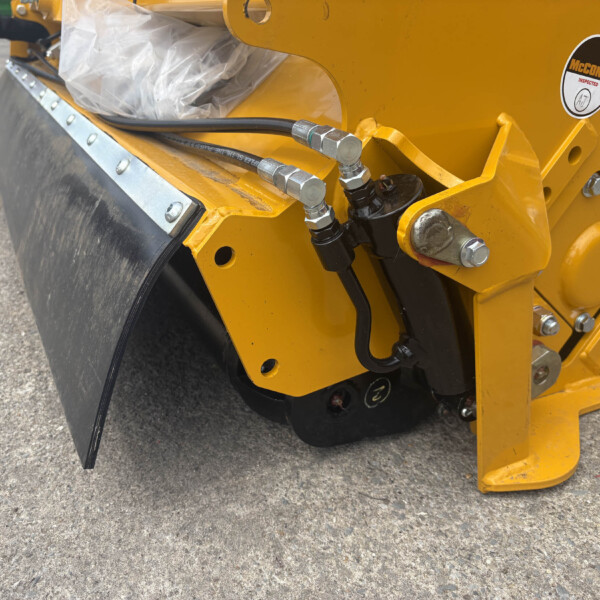 Close-up of yellow construction machine showing hydraulic hoses, metal fittings, and bolts
