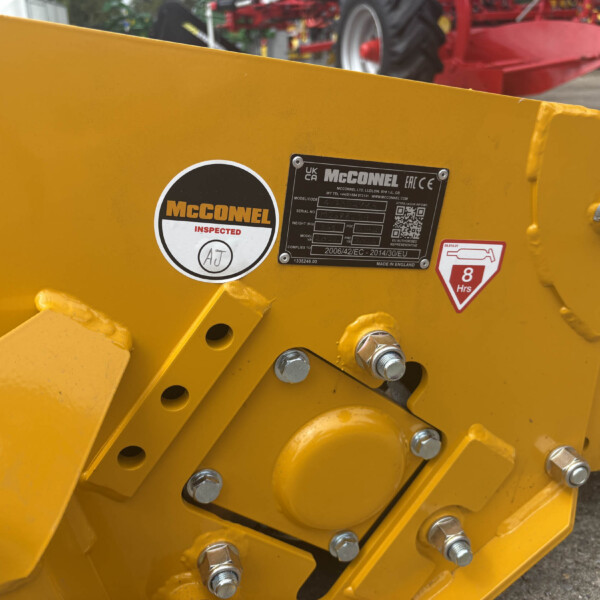 Close-up of bright yellow agricultural machinery with exposed bolts and a McConnel label plate.